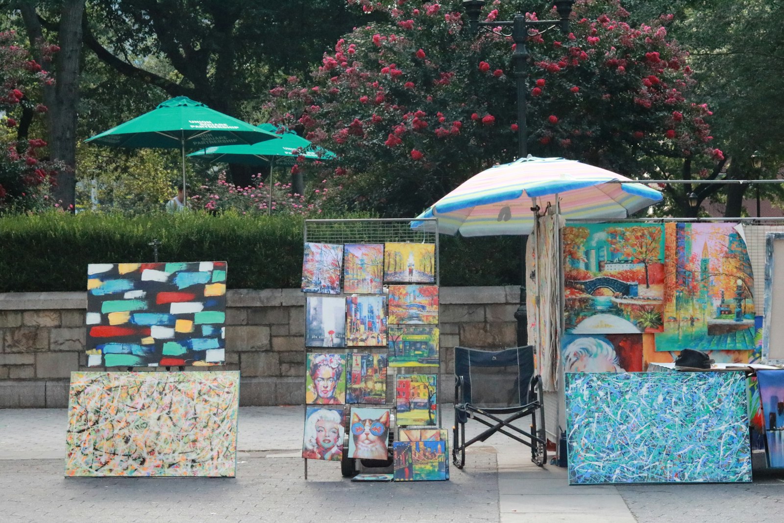 Colorful paintings displayed at an outdoor art market beneath umbrellas