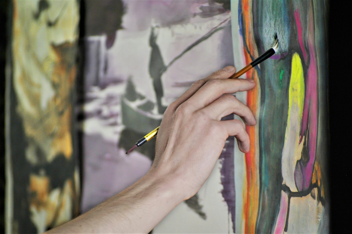 An artist’s hand holding a brush while painting a colorful canvas